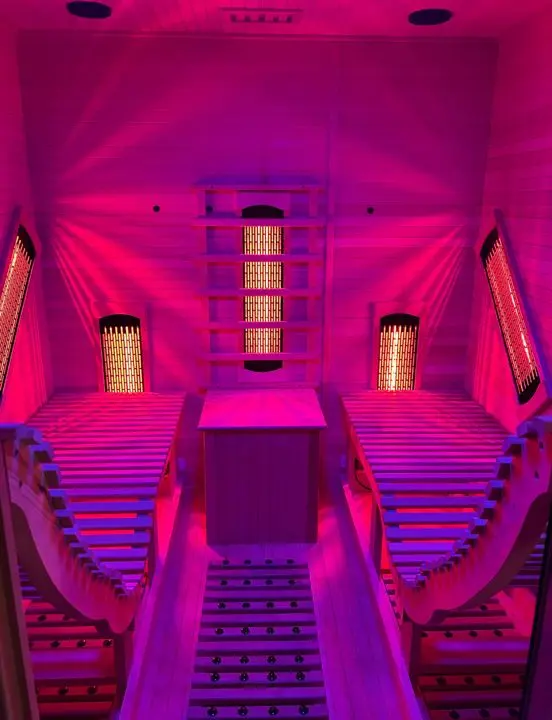 Inside the lay-down infrared sauna at AND Wellness, with two reclined loungers glowing in warm pink light